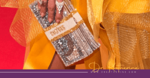 Close up of a glittery bag styled as a wad of cash. A woman's yellow dress and hand can be seen in-shot. A purple footer can be seen with the Dr. Katherine signature in yellow and www.drkatherine.com underneath that