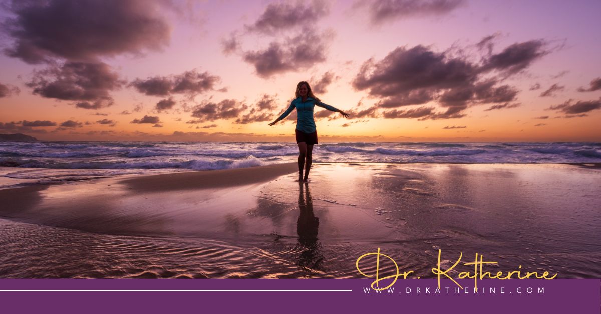 Photo of a women standing on the beach with her arms outstretched. A purple footer can be seen with the Dr. Katherine signature in yellow and www.drkatherine.com underneath that