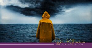 Photo of a person in a yellow rain coat looking out to a stormy sea. A purple footer can be seen with the Dr. Katherine signature in yellow and www.drkatherine.com underneath that